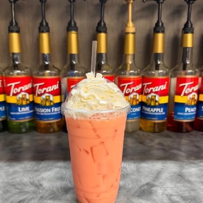 A peach-colored Red Bull infusion drink with whipped cream in front of Torani syrup bottles